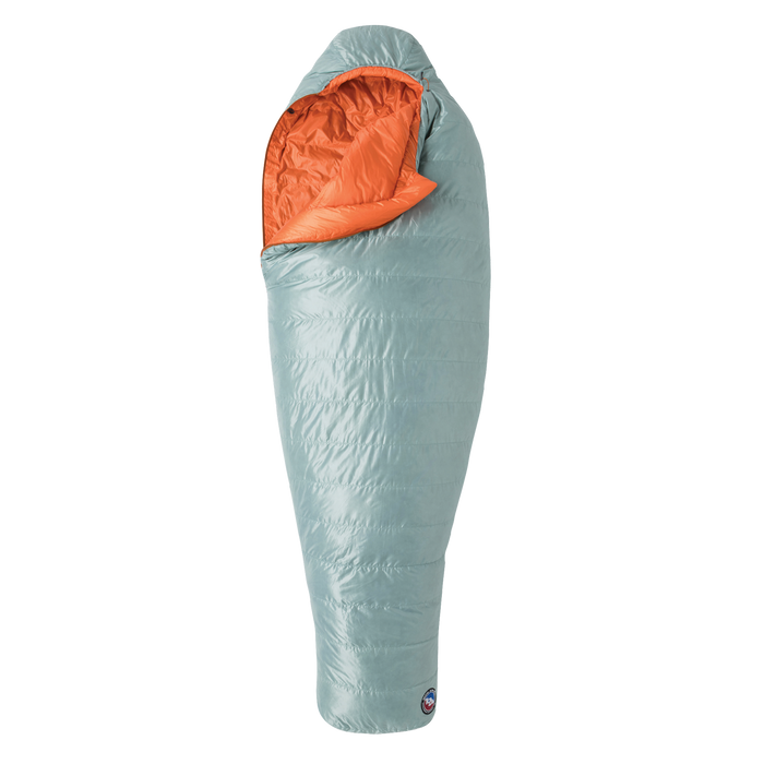 The Big Agnes Returns Women's Greystone 30° sleeping bag in light blue, featuring DownTek insulation, stands upright against a white background. Its mummy-style hood is slightly open, showing the bright orange interior lining.