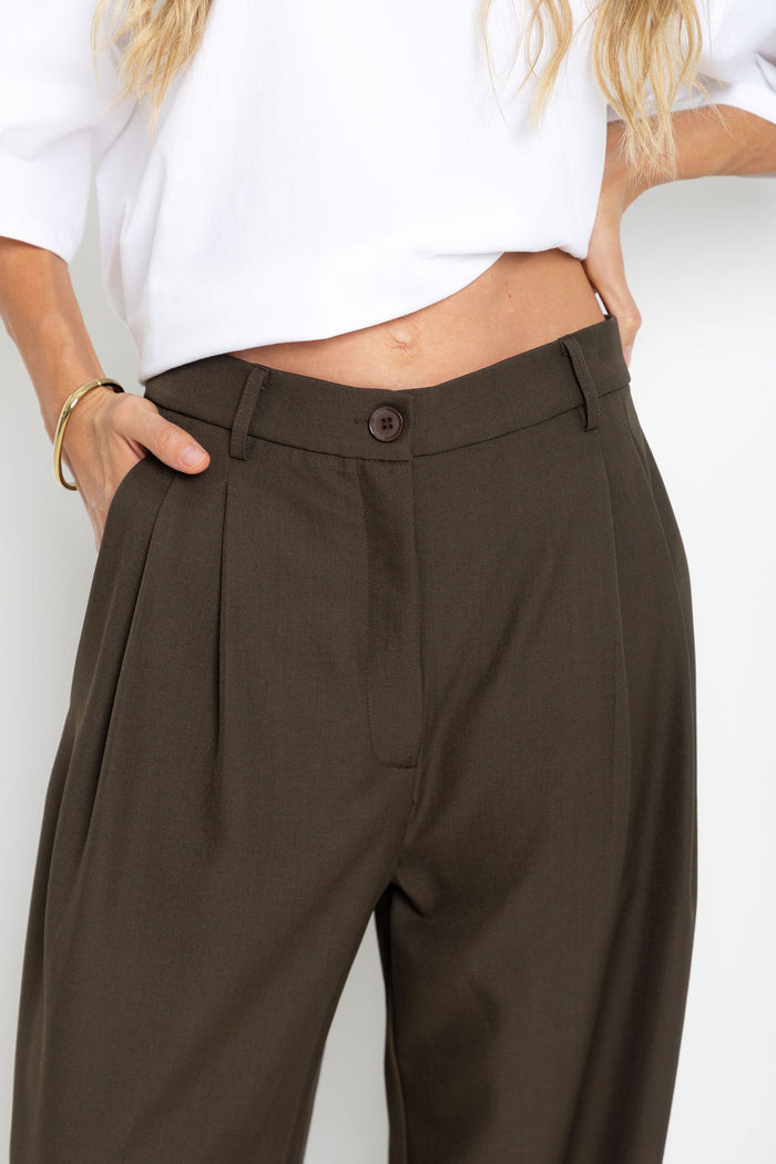 Xavier pants in dark olive brown – high-waisted, wide-leg trousers with pleated front, worn with a white cropped tee and thong sandals